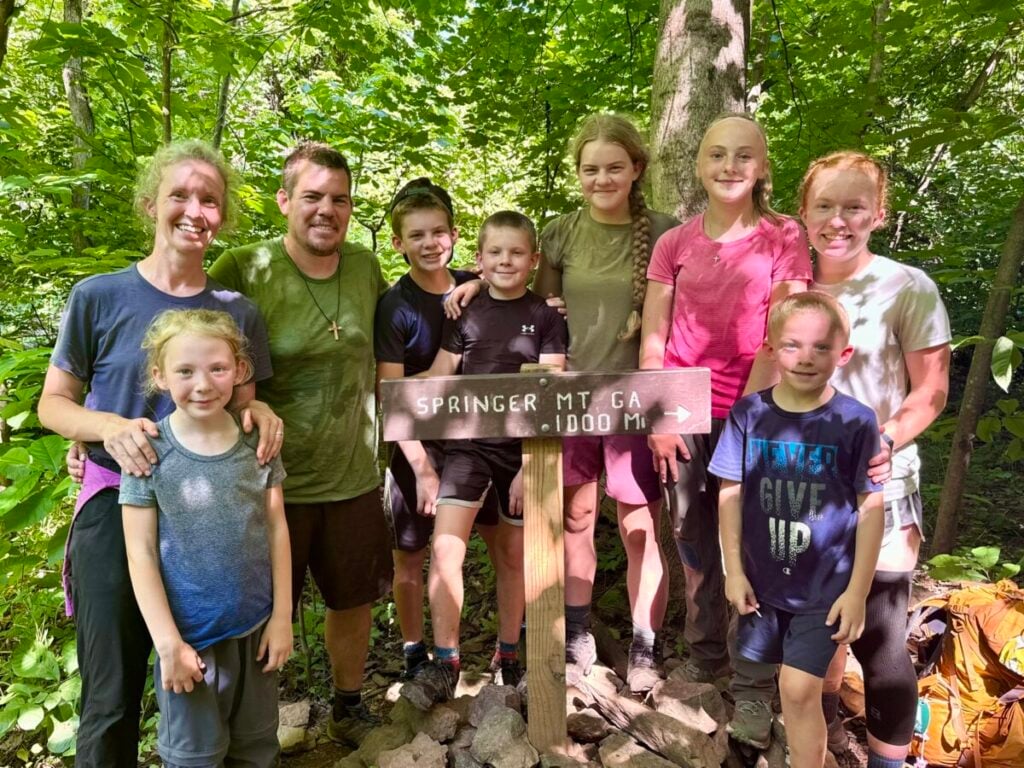 A large family poses with a 1000 mile sign on the Appalachian Trail.