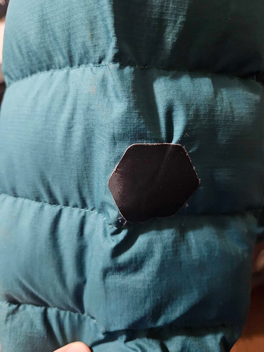 Teal jacket with a black hexagonal patch.