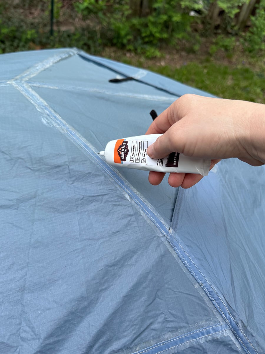 Seam sealant being used to re-seal the seams on a blue tent.