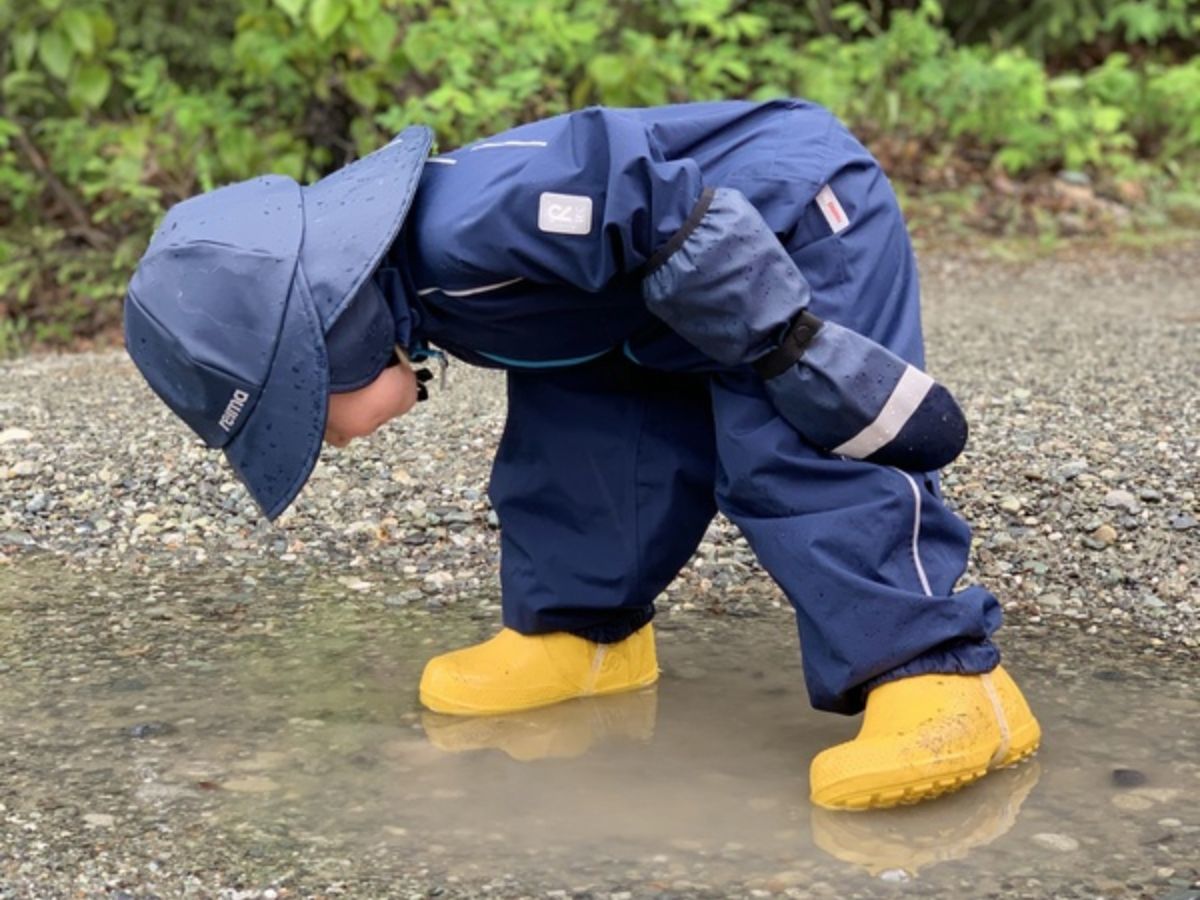 ReimaRainJumpsuit A young child in Reima rain gear looks down into a puddle.
