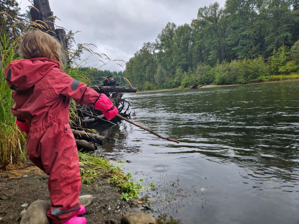 A girl in a rain suit plays near a river.