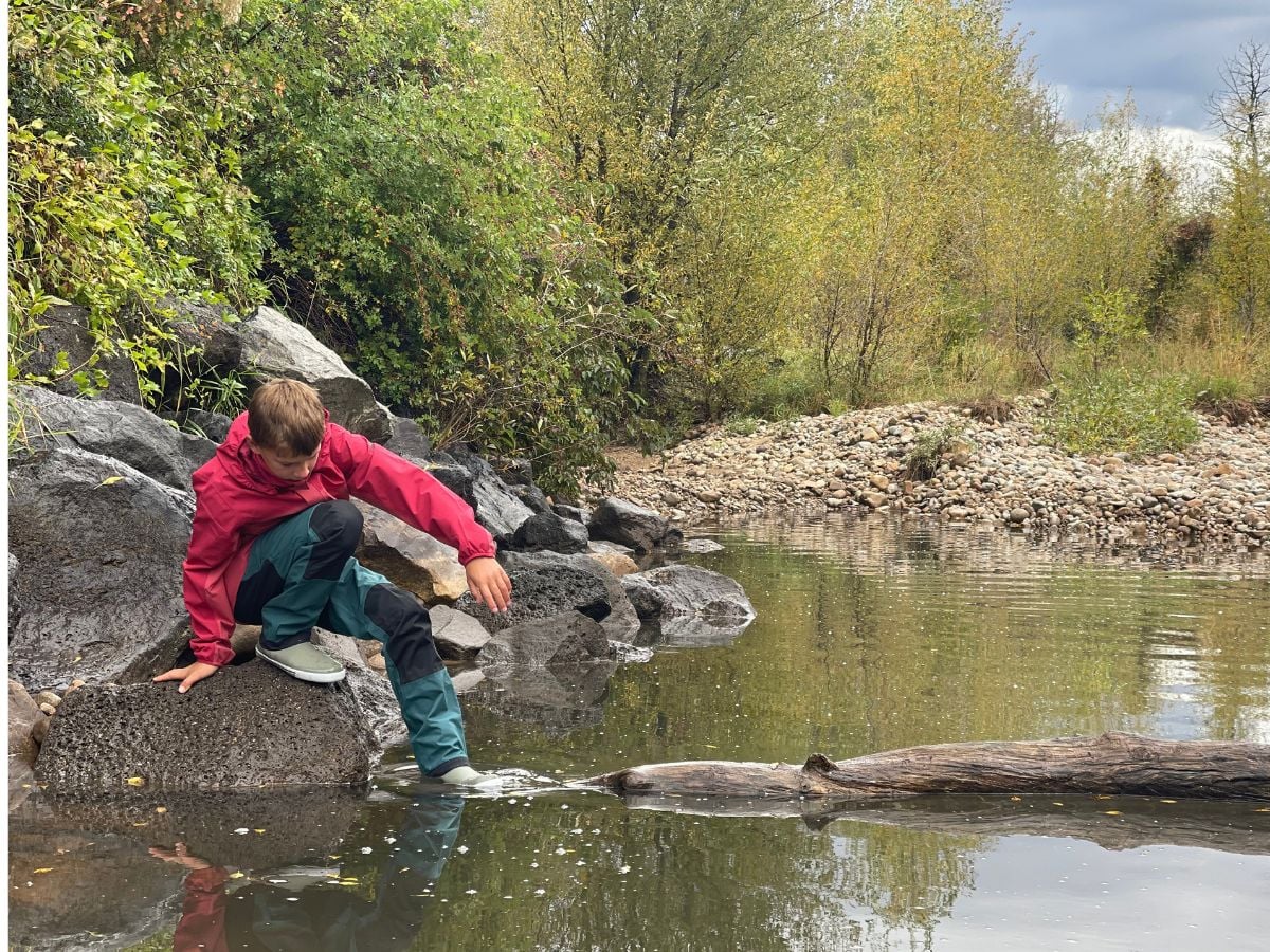 boy sits on a boulder near a creek surrounded by fall colors.