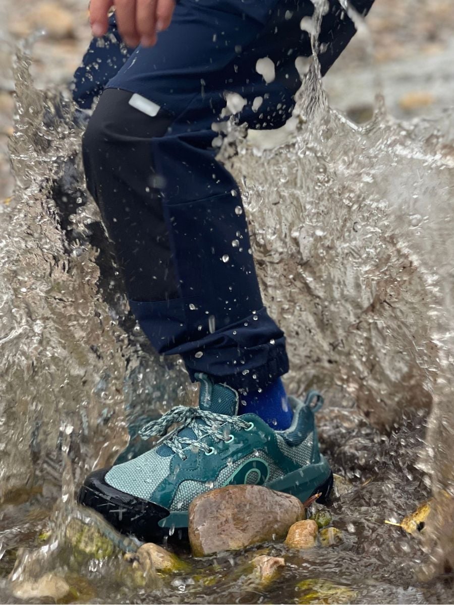 A leg and foot of a child splashing in a puddle in waterproof gear.