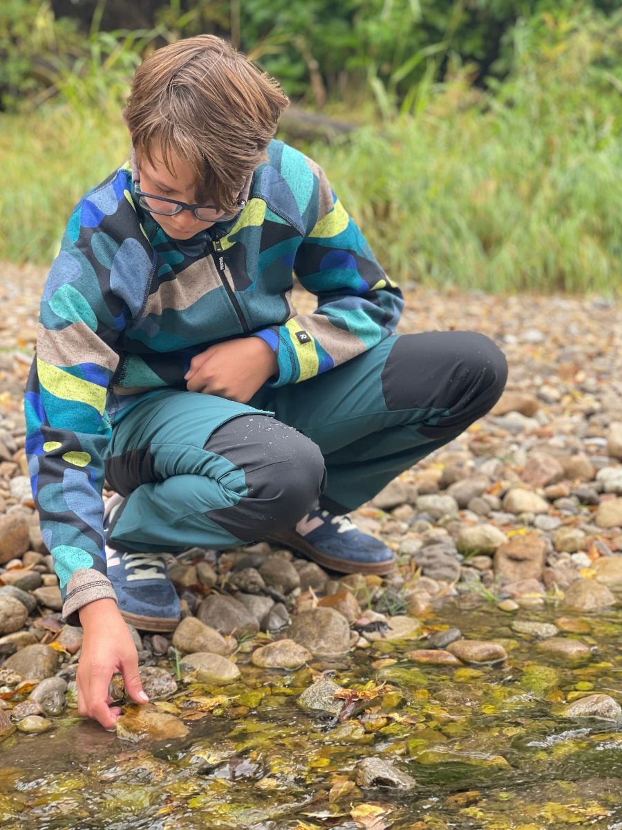 A boy inspects rocks in a creek, wearing Reima fleece and pants.