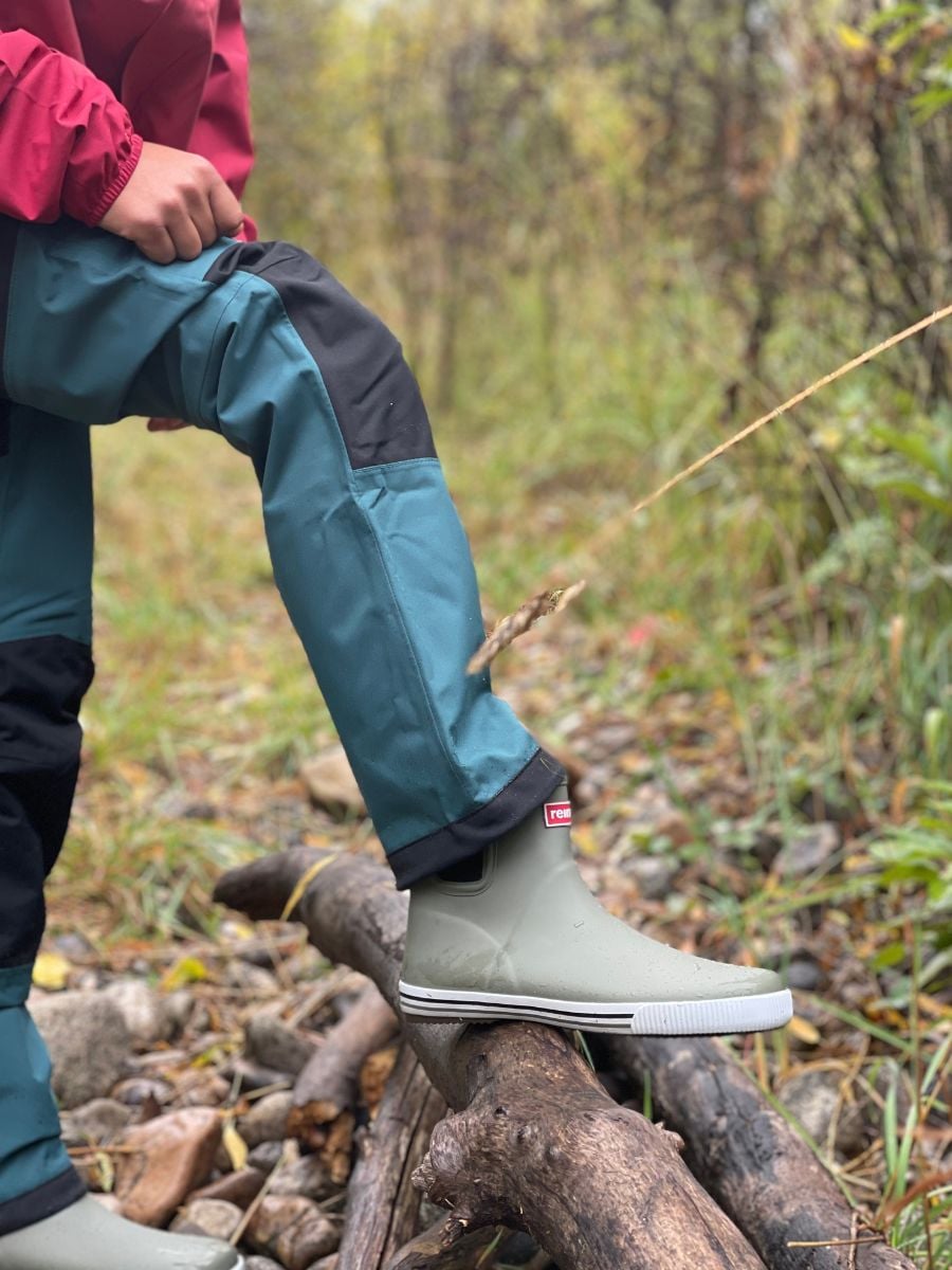A leg and a boot dressed in rain pants and a gray rain boot.
