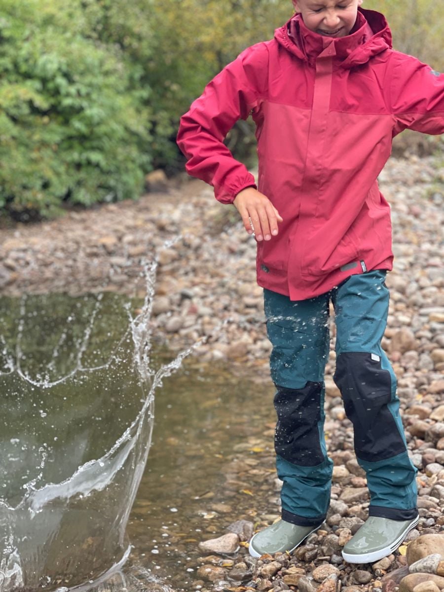 A boy winces as he throws a rock into a pond, getting splashed.