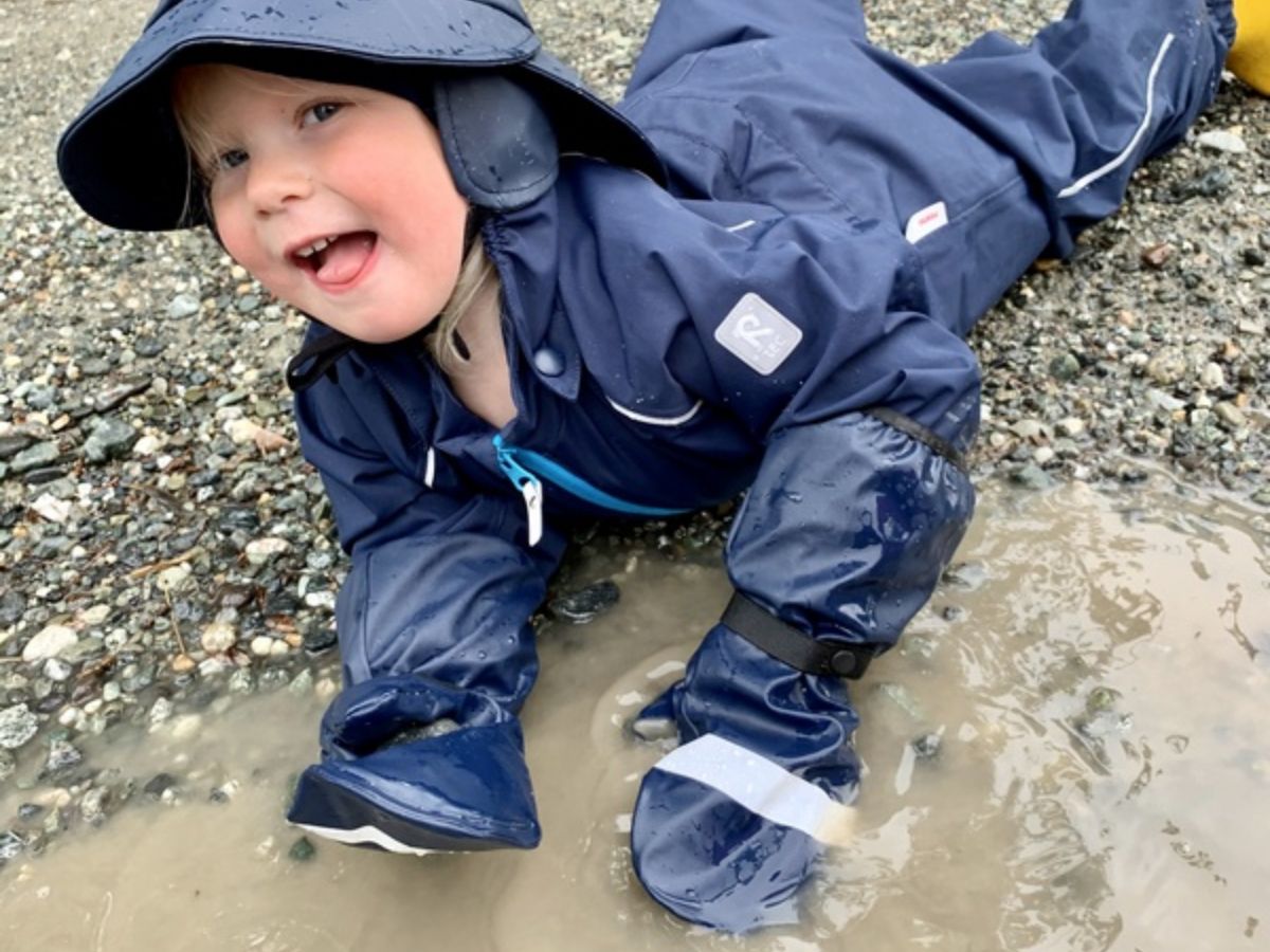 reimarainmittens A young child in navy blue reima rain mittens, hat and rain suit.